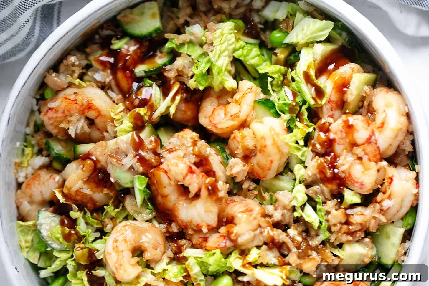 A beautifully presented serving bowl filled with Teriyaki shrimp, crispy rice, cucumber, edamame, and fresh lettuce.