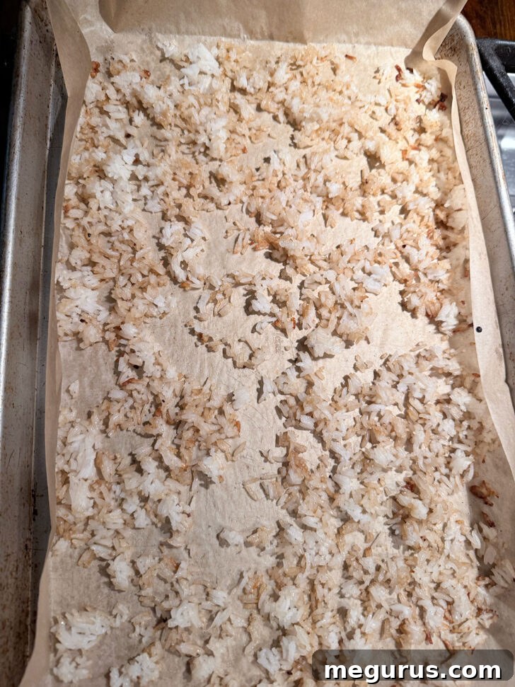Cooked rice seasoned with teriyaki sauce and sesame oil spread on a parchment-lined baking sheet, ready for crisping.
