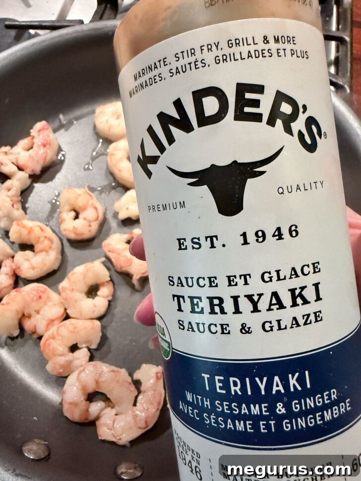 Shrimp cooking in a skillet, with teriyaki sauce being added to coat them.