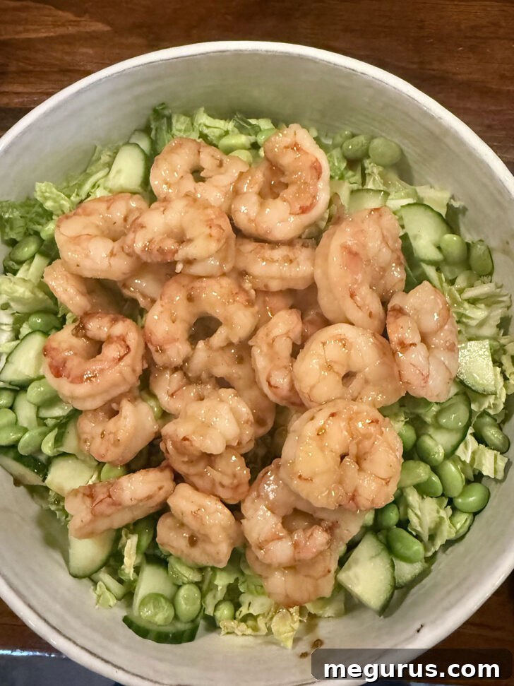 Cooked teriyaki shrimp being spooned over the dressed salad in a bowl.
