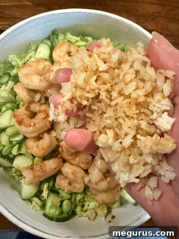 Crispy rice being added to the salad bowl with shrimp and greens.