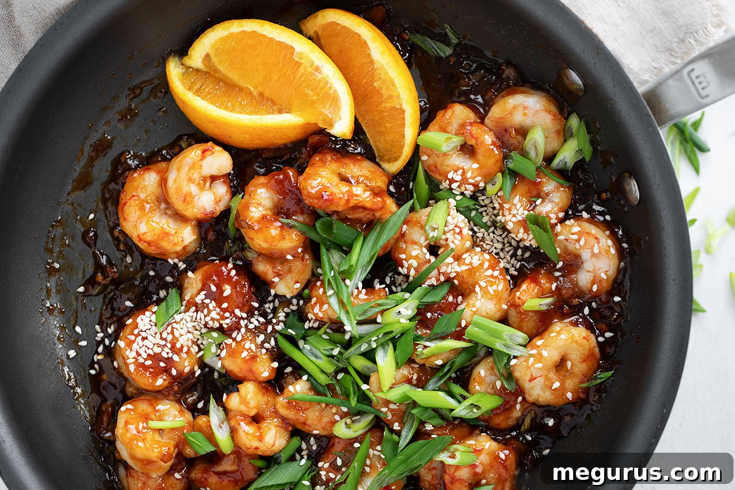 Spicy orange shrimp sizzling in a hot skillet, garnished with fresh herbs.
