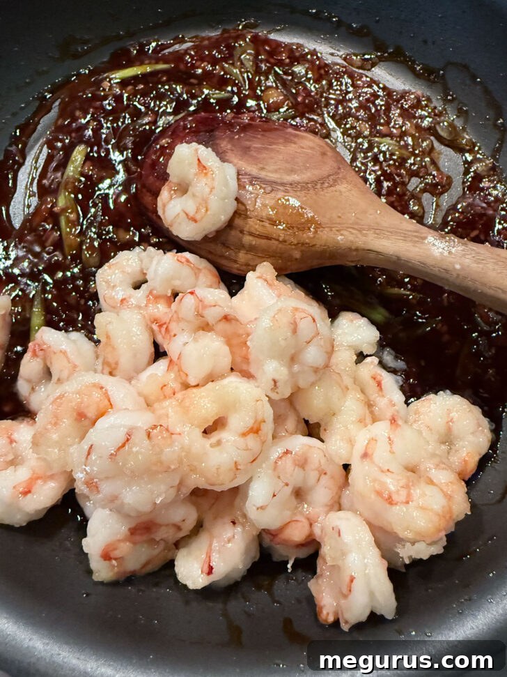 Adding the cooked shrimp to the skillet with the spicy orange sauce.