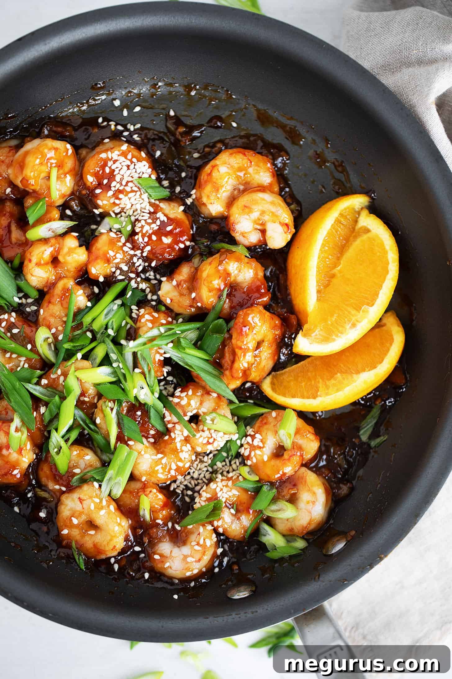 Spicy orange shrimp served in the skillet with fresh orange wedges and green onions.