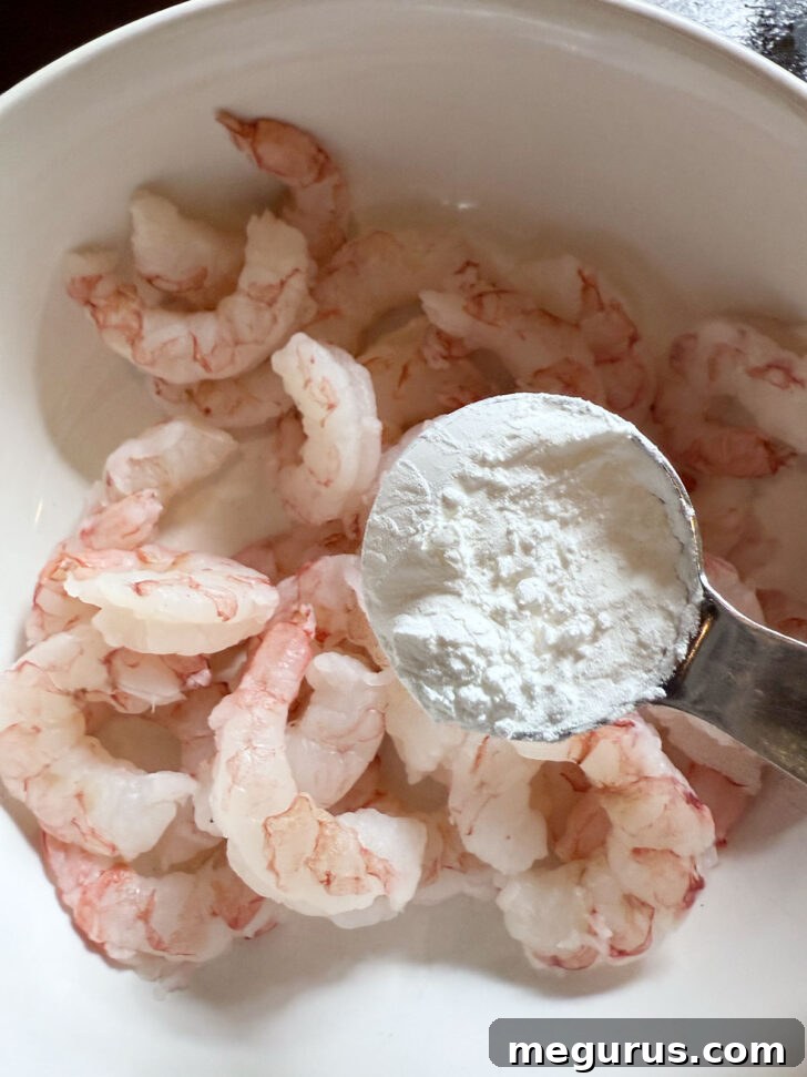 Adding cornstarch to the shrimp in a bowl.