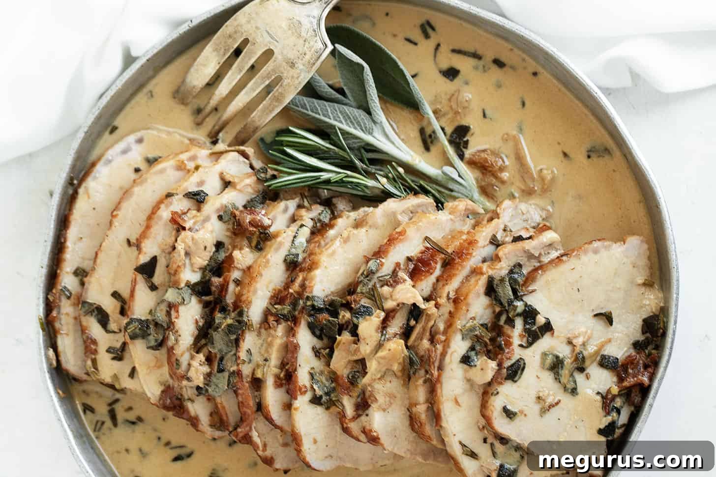 Juicy pan-seared pork loin with creamy wine and herb gravy, sliced and served on a platter with a fork, garnished with fresh herbs.