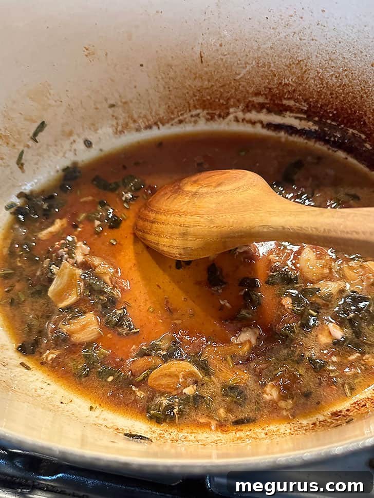 Stirring chicken broth into the pan to scrape up and incorporate all the flavorful browned bits.