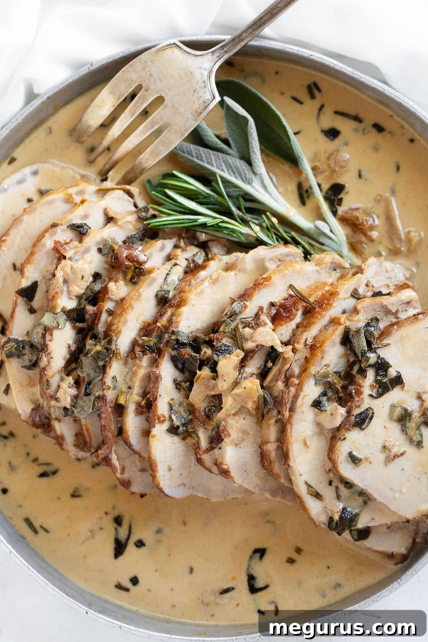 Platter of thinly sliced pork loin with a generous pour of creamy wine and herb gravy, garnished with fresh herbs, ready to be served.