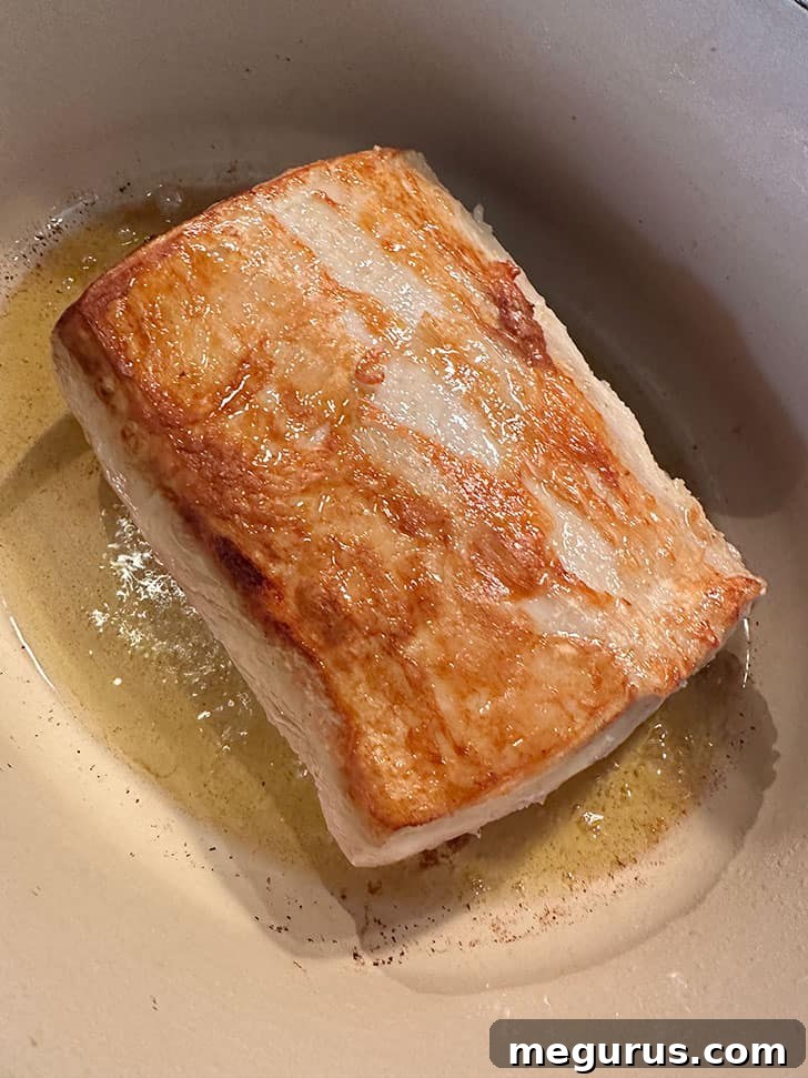 Browning the pork loin on one side in hot olive oil in a Dutch oven.