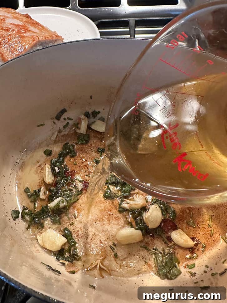 Adding white wine to sautéed garlic and fresh herbs in the pan after removing the pork.