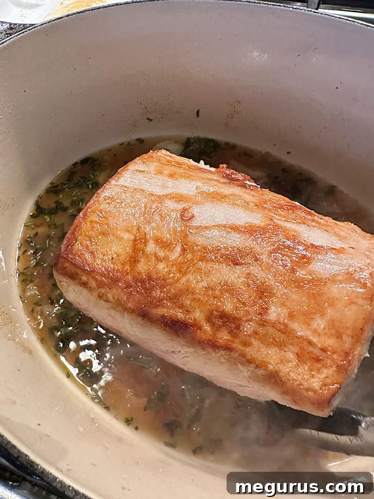 Returning the browned pork loin roast to the pan with the wine, garlic, and herbs.