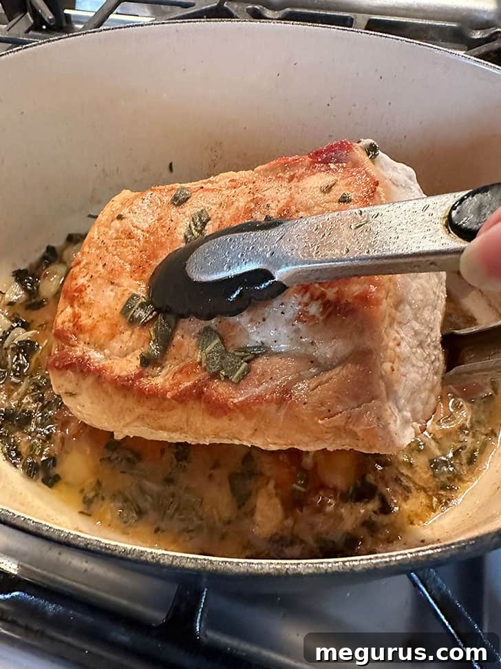 Flipping the pork loin in the pan to ensure even cooking and browning on all sides.