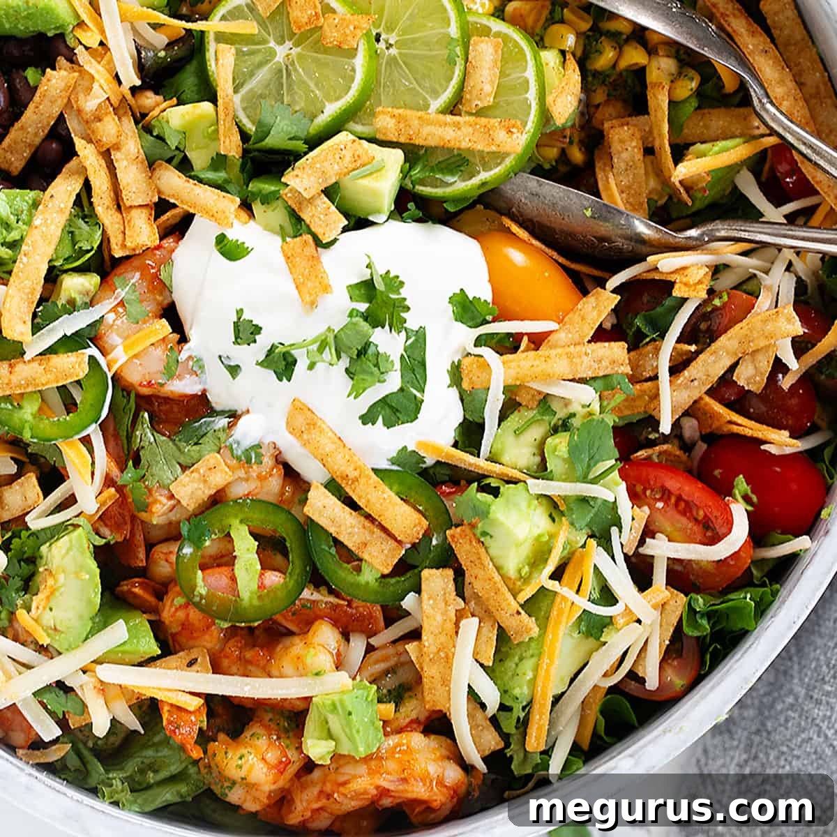Shrimp taco salad in a large bowl with serving tongs, featuring corn, black beans, and avocado.