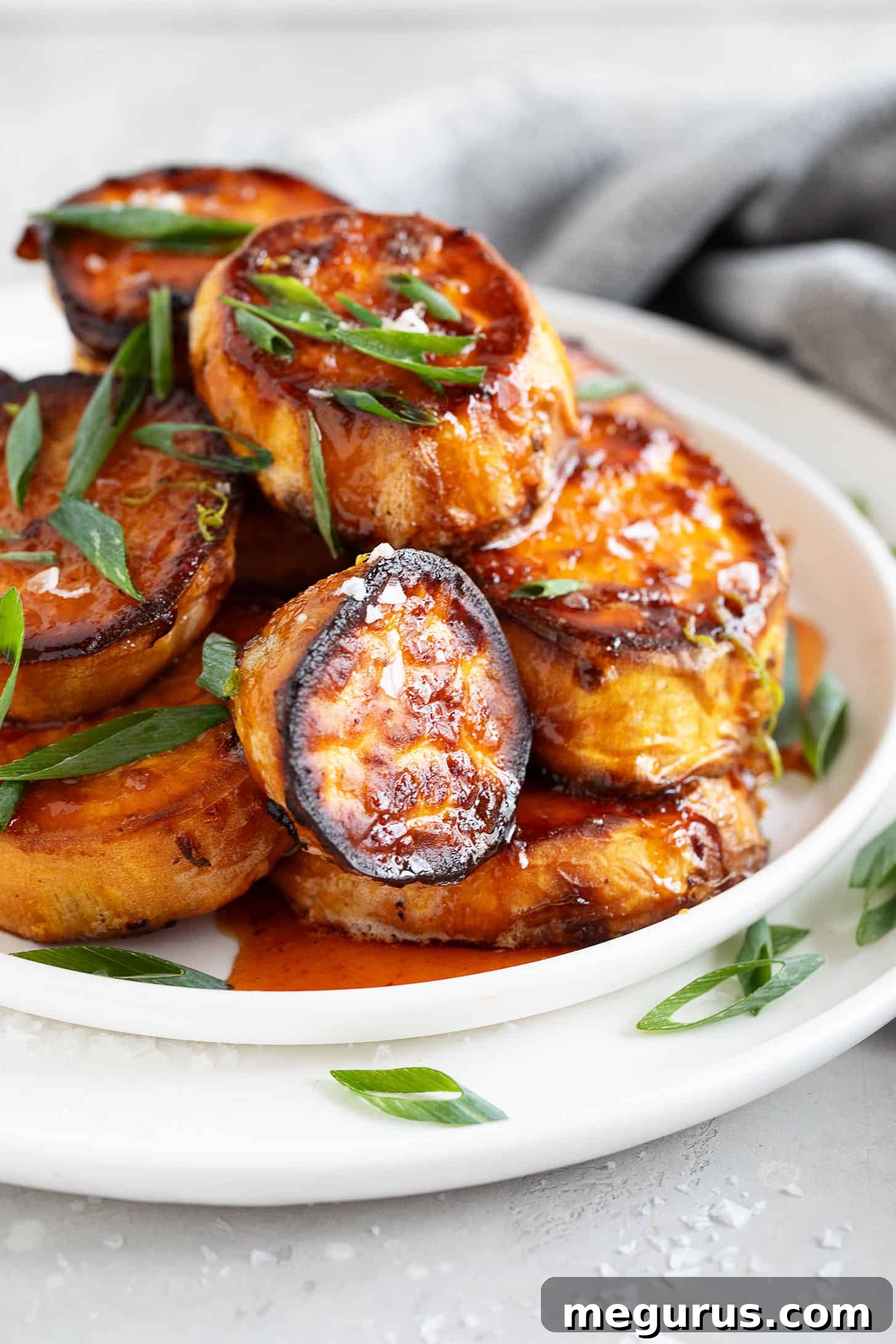 A large serving platter piled high with honey sriracha melting sweet potatoes, garnished with green onions and flaky salt, ready to be shared.