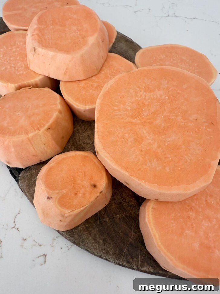 Sweet potatoes peeled and uniformly sliced into 1-inch thick rounds on a wooden cutting board, ready for roasting.