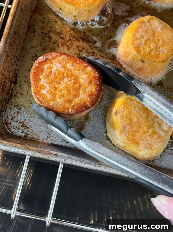 Sweet potato slices being flipped on the baking sheet with tongs halfway through the roasting process to ensure even browning on both sides.