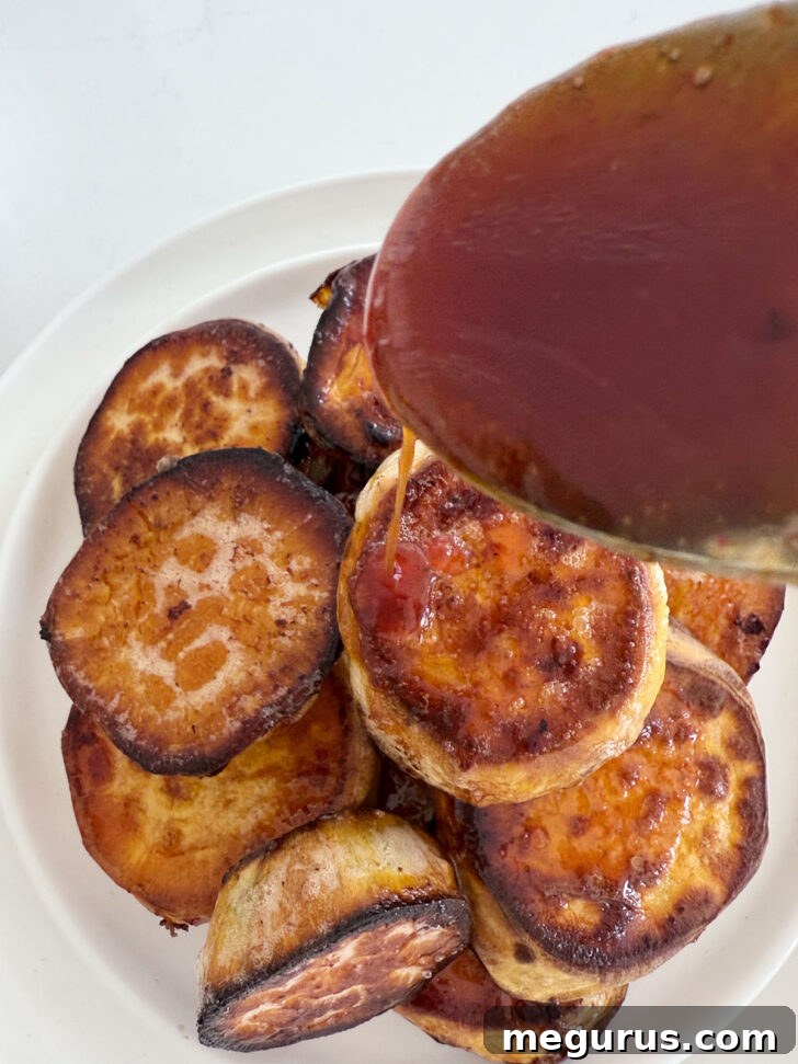More honey sriracha sauce being generously drizzled over a stack of freshly roasted melting sweet potatoes on a serving plate.