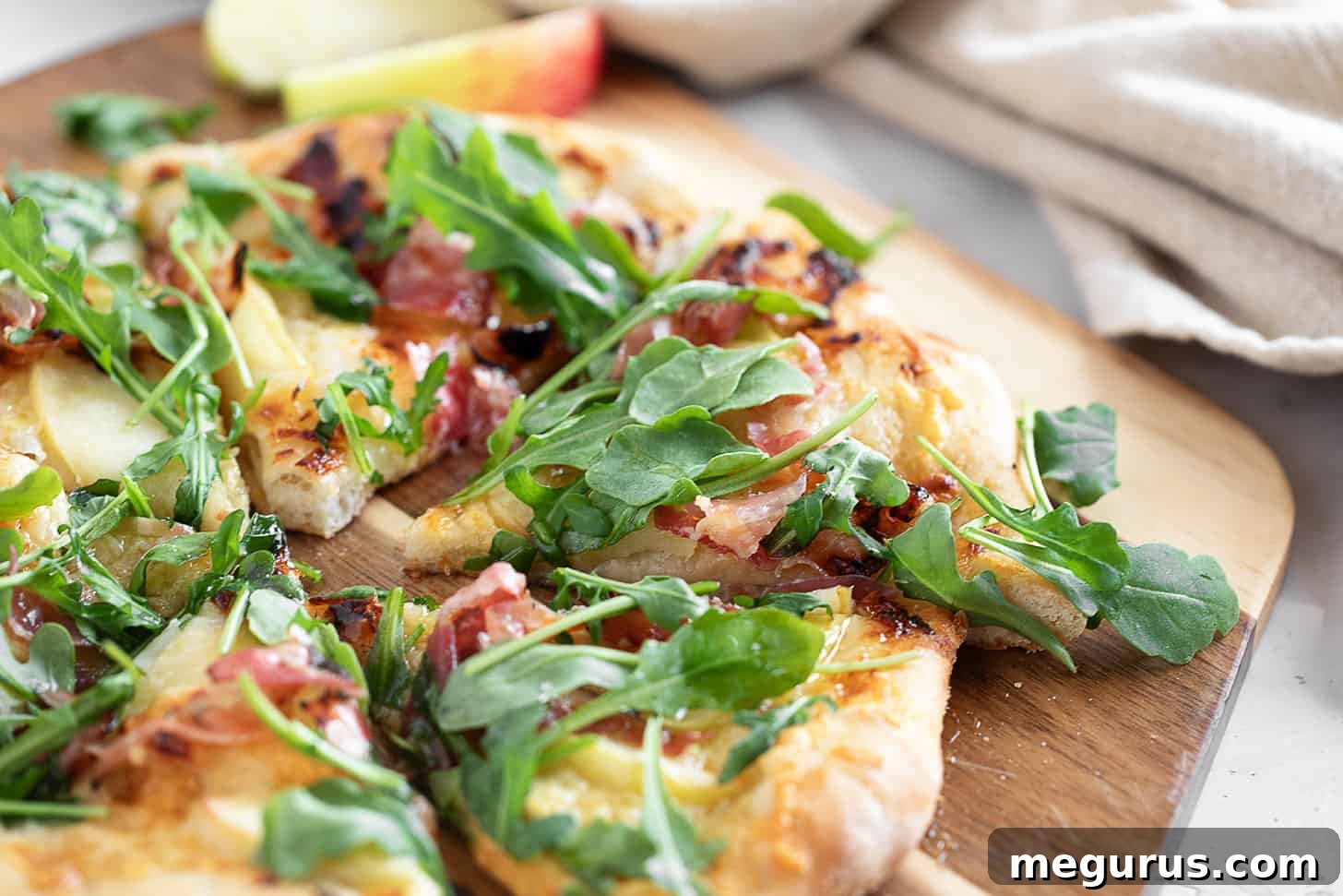 Apple cheddar and pancetta pizza on pizza peel, showcasing its golden crust and delicious toppings.