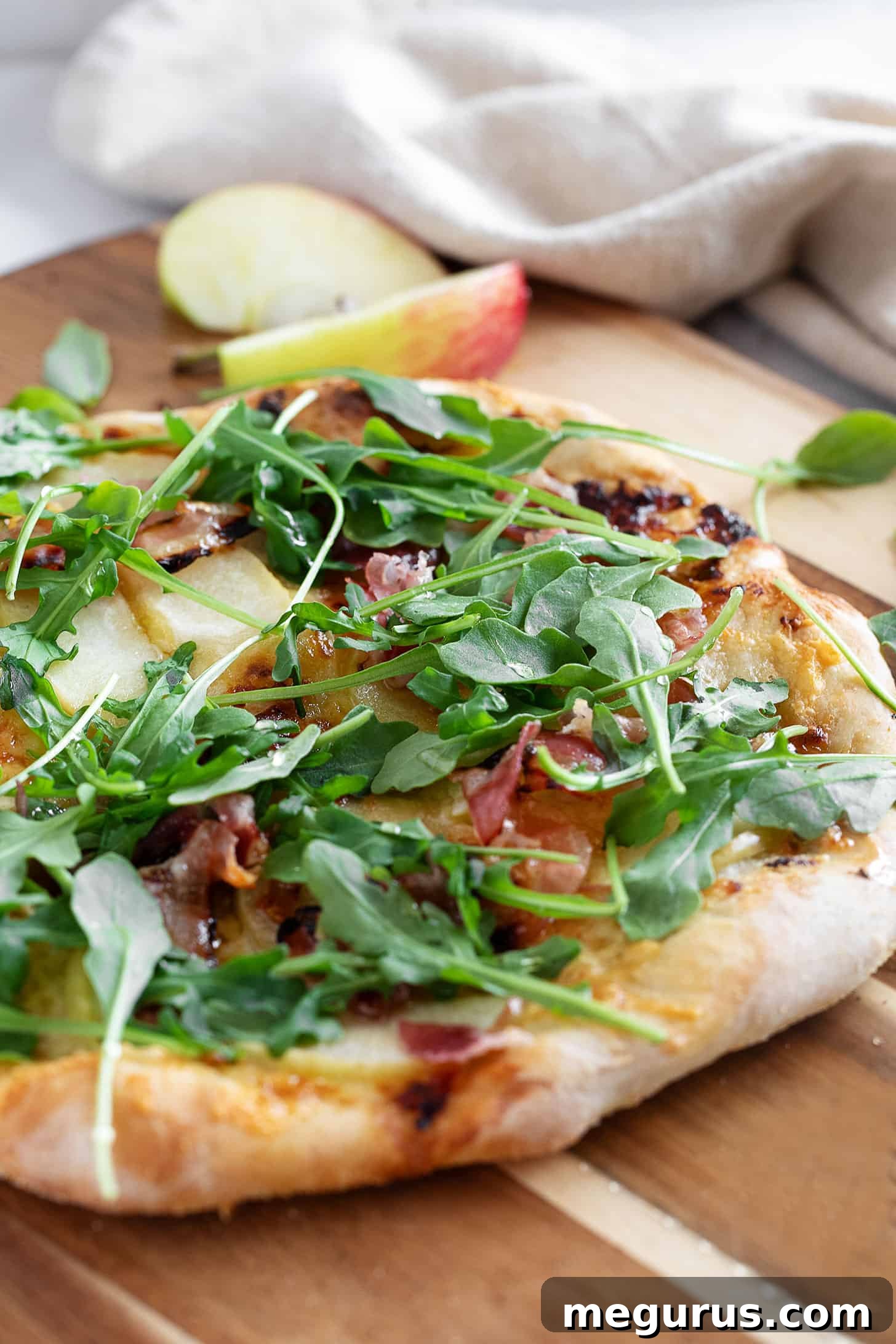 Apple cheddar and pancetta pizza on pizza peel, garnished with fresh arugula and a final honey drizzle.