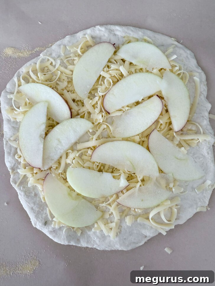 Pizza dough topped with shredded smoked cheddar and apple slices.
