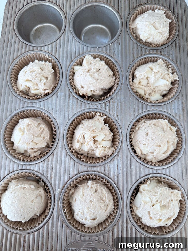Apple muffin batter scooped into muffin cups.