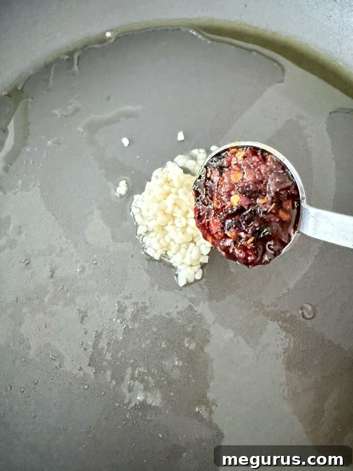 Adding garlic and chili crisp to a hot skillet with oil.