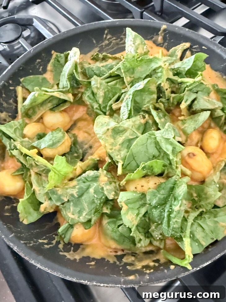 Adding the spinach to the gnocchi in the skillet.