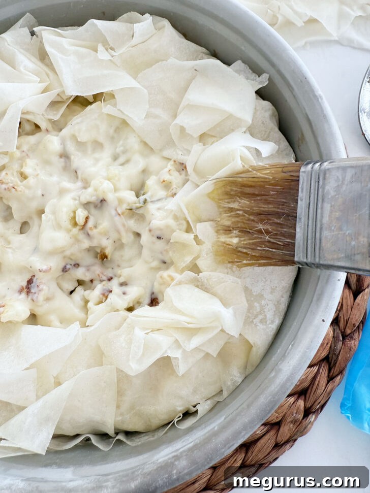 Brushing the ruffled phyllo top of the pie with melted butter to ensure a golden crust.