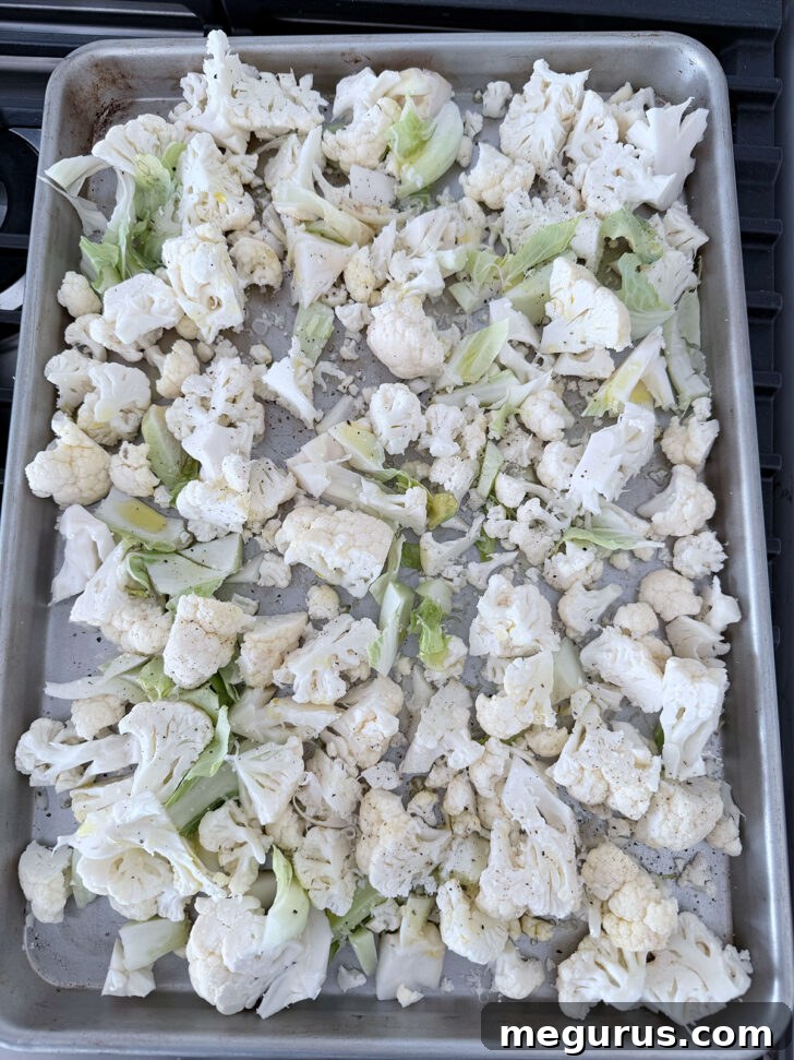 Chopped cauliflower, including core and leaves, spread on a baking sheet before roasting.
