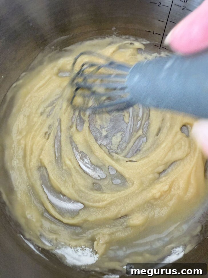 Whisking together butter and flour in a saucepan to create a roux for the cheese sauce.