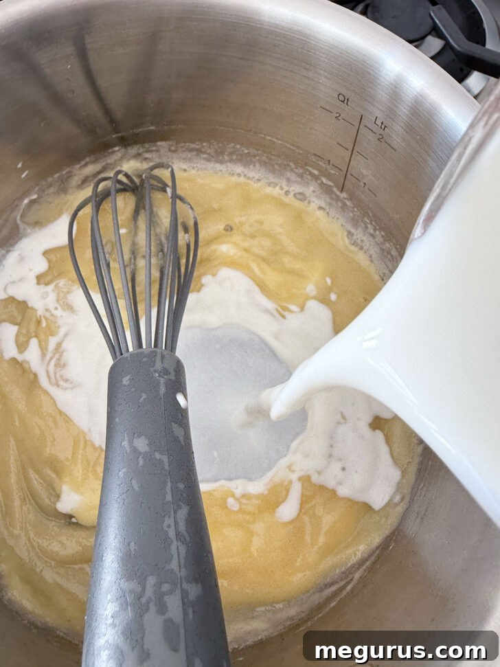 Gradually adding milk to the roux in a saucepan for the cheese sauce.