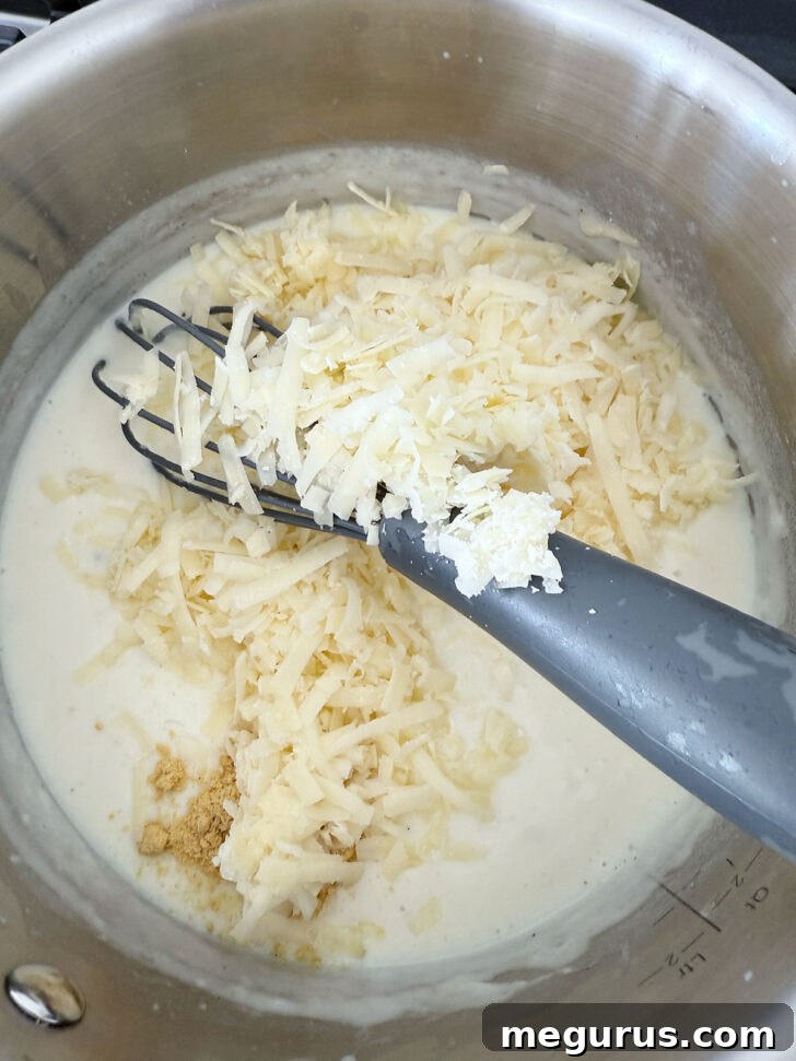 Adding dry mustard and shredded cheddar cheese to the thickened sauce, ready to whisk until smooth.