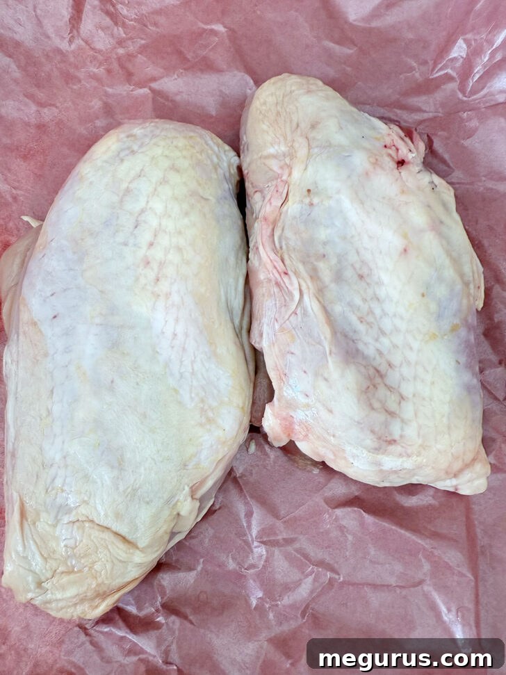 Two boneless, skin-on chicken breasts seasoned with salt and pepper, ready for cooking.