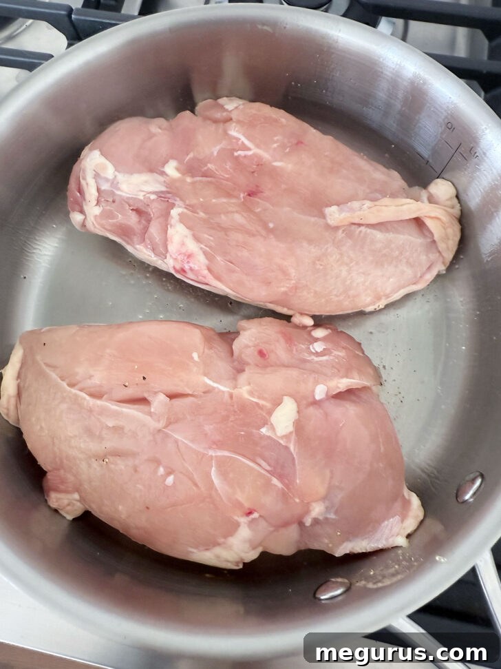 Chicken breasts searing skin-side down in a hot skillet, developing a golden-brown crust.