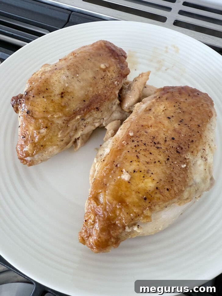 Glazed chicken breasts resting on a plate after being removed from the skillet.