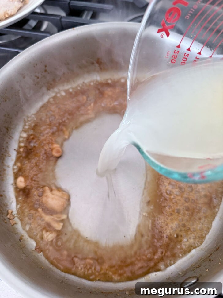 Pouring chicken broth into the skillet to deglaze and start the pan sauce.