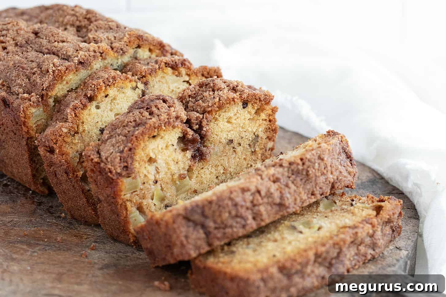 A freshly baked Dutch apple loaf, beautifully sliced on a wooden cutting board, revealing its tender crumb, visible apple pieces, and golden-brown, crumbly topping.