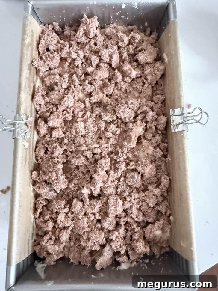 The apple loaf batter is in the baking pan, topped with a generous layer of crumb mixture, ready for the oven.