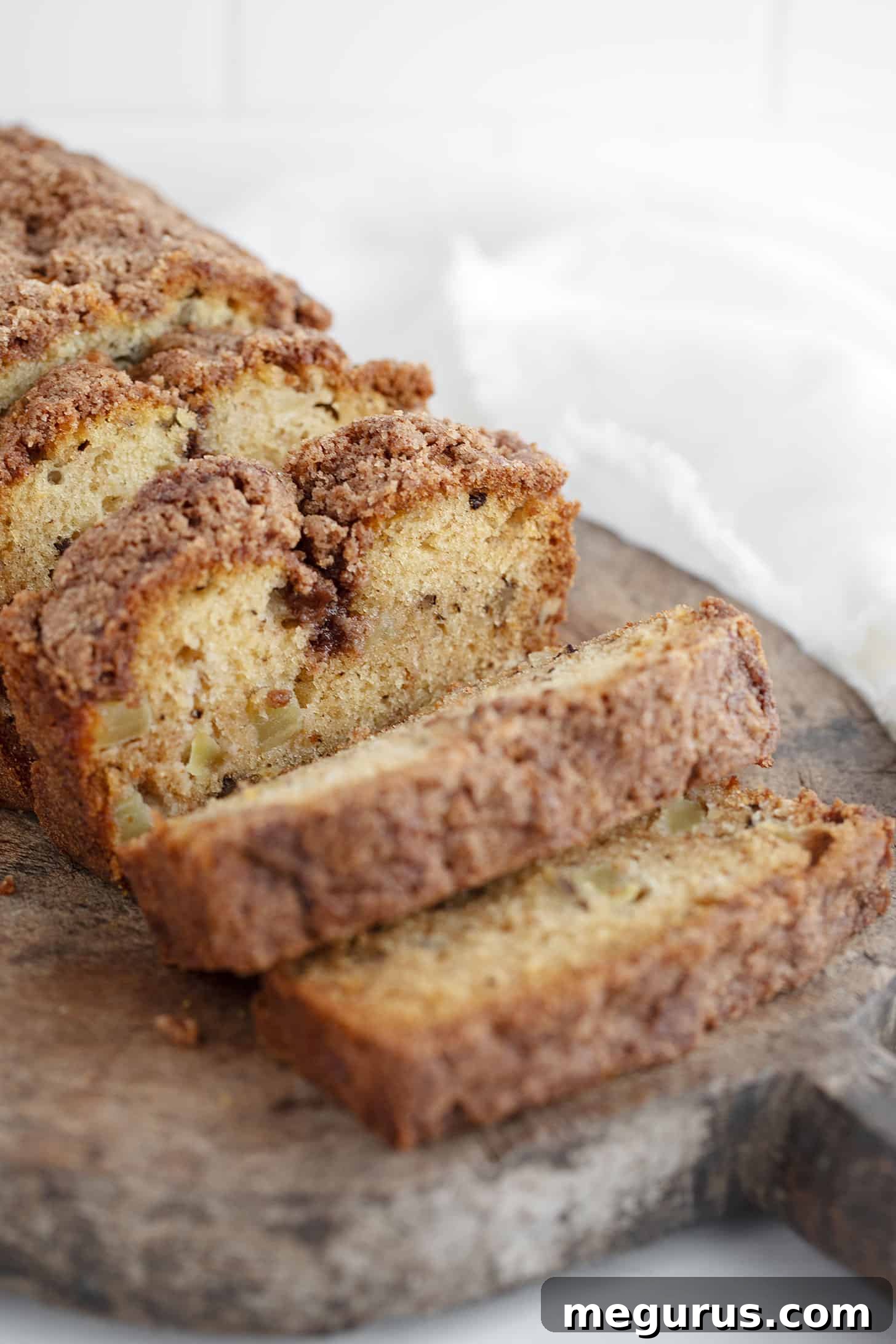 A close-up shot of a perfectly baked Dutch apple loaf, sliced to reveal its moist interior, chunks of apple, and a crisp cinnamon crumb topping.