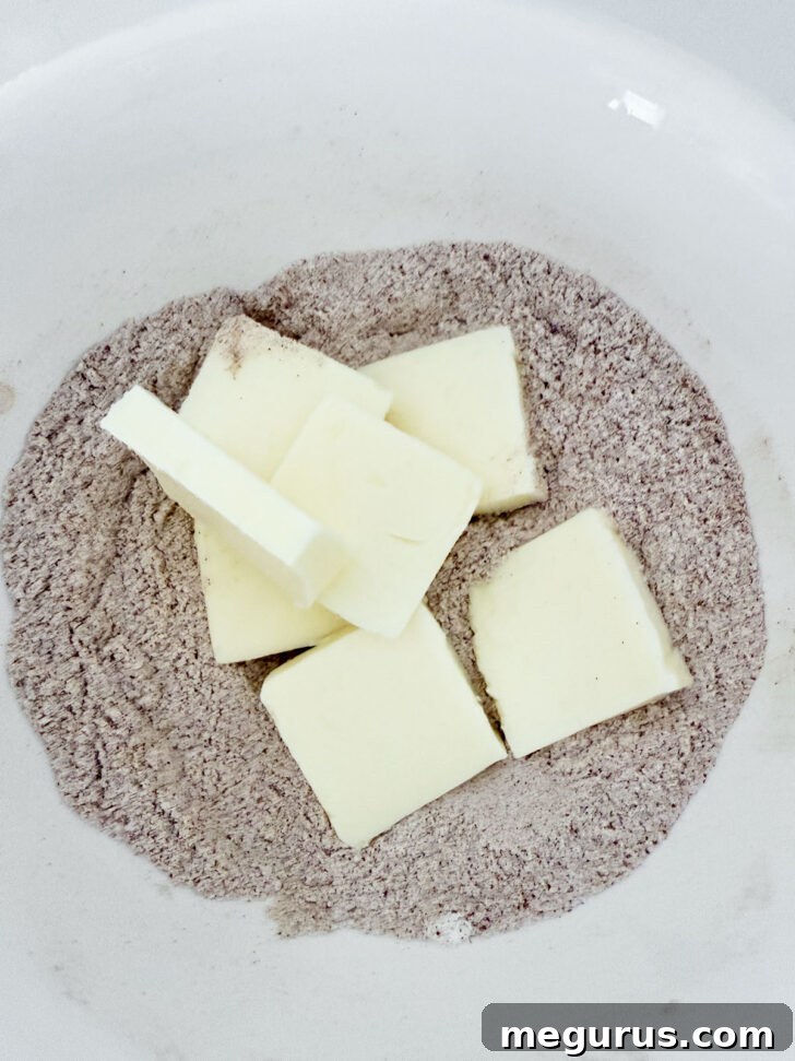 Cold butter cubes are being added to a bowl containing sugar and cinnamon, ready to be mixed for the crumb topping.