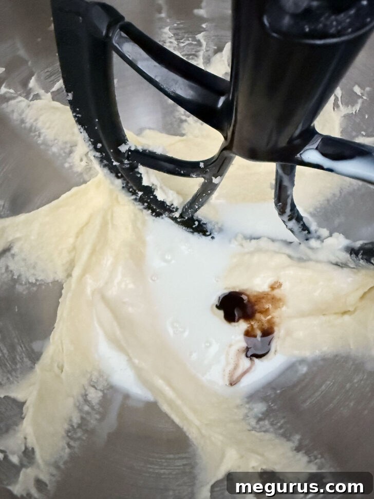 Vanilla extract is being poured into the batter, which is in a mixing bowl.