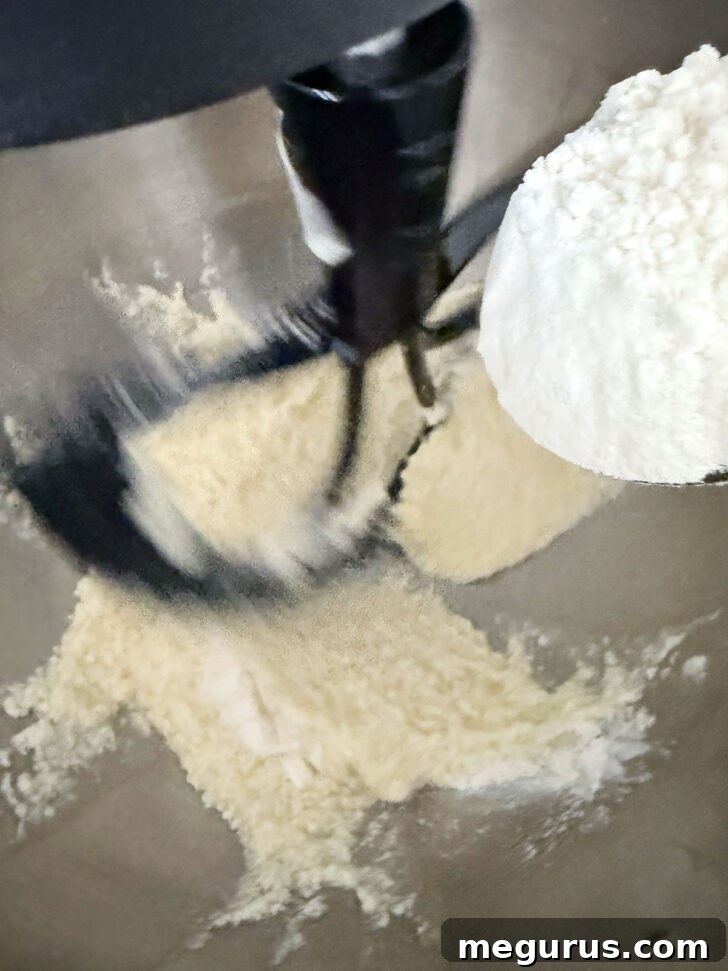 The dry flour mixture is being slowly added to the wet batter in a mixing bowl, ready to be combined.