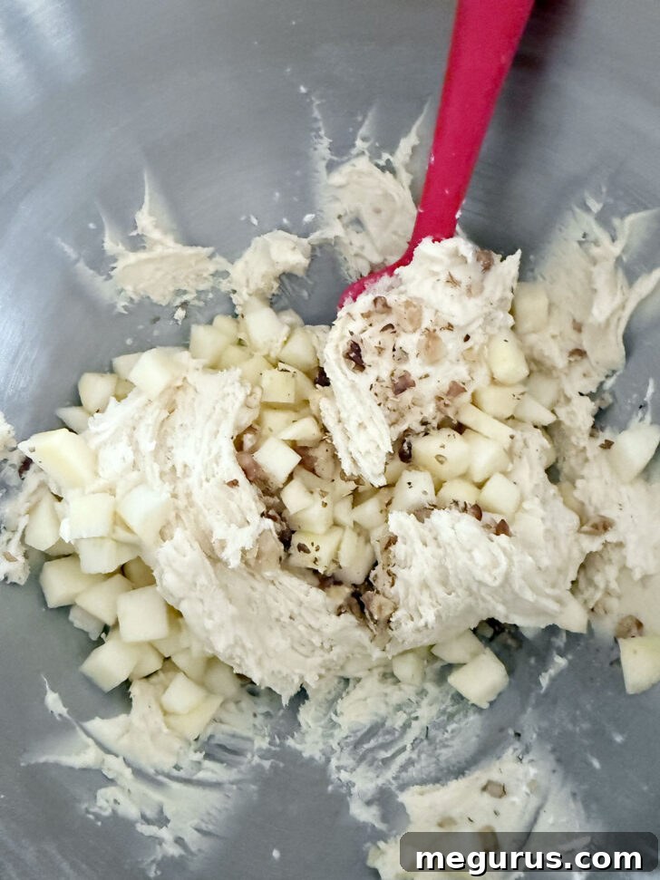 Diced apple pieces are being added to the loaf batter, ready to be folded in.