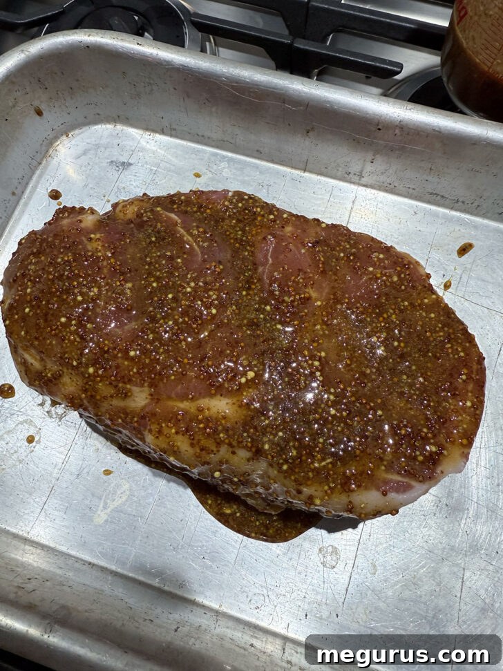 Maple mustard pulled pork in a roasting pan ready for the oven, generously coated in glaze.