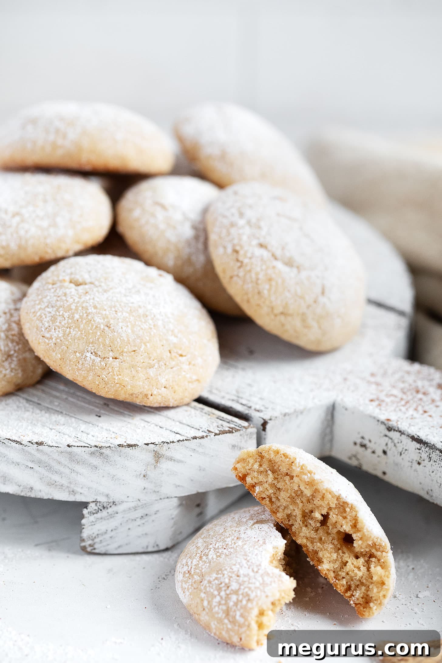 A close-up of freshly baked brown butter cinnamon cookies, some dusted with extra icing sugar, on a cooling rack.