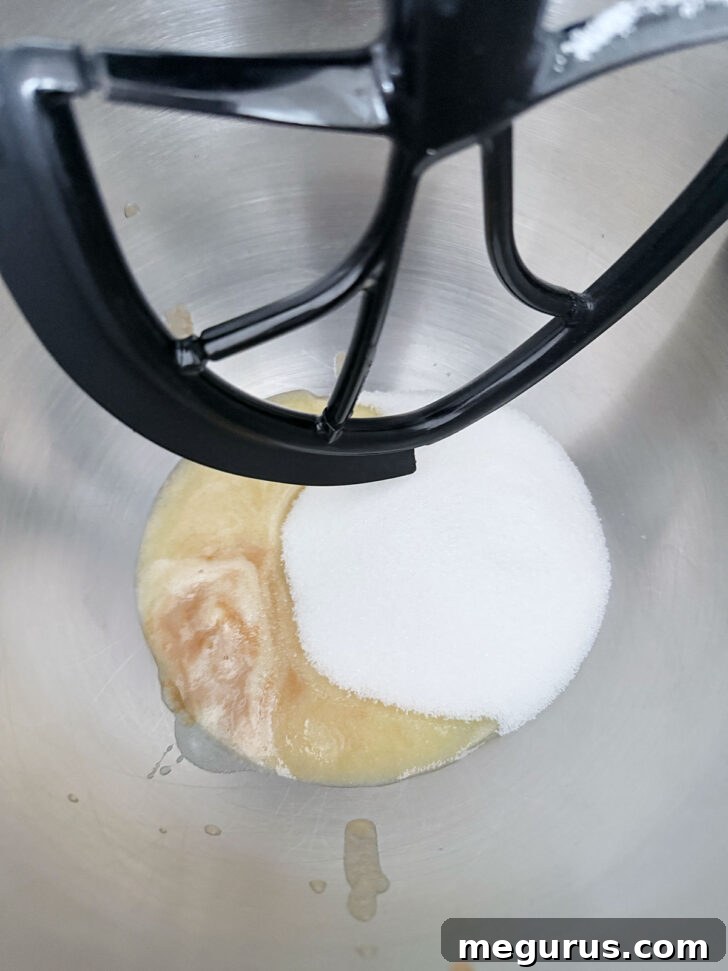 Cooled brown butter and various sugars being combined in the bowl of a stand mixer.