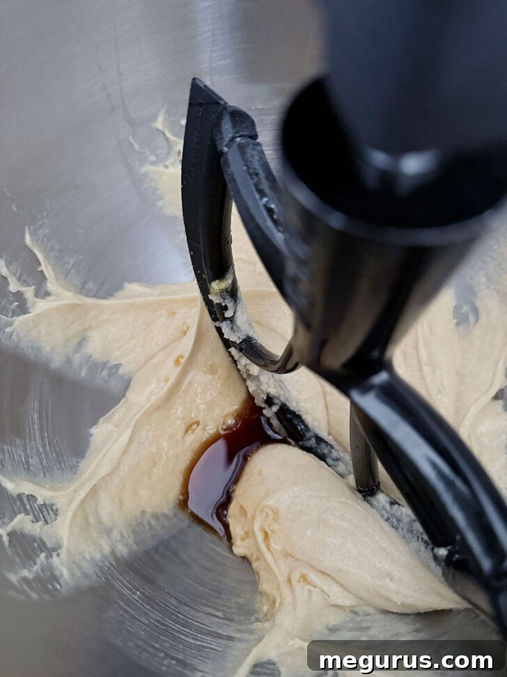 Vanilla extract being poured into the creamed brown butter and sugar mixture.