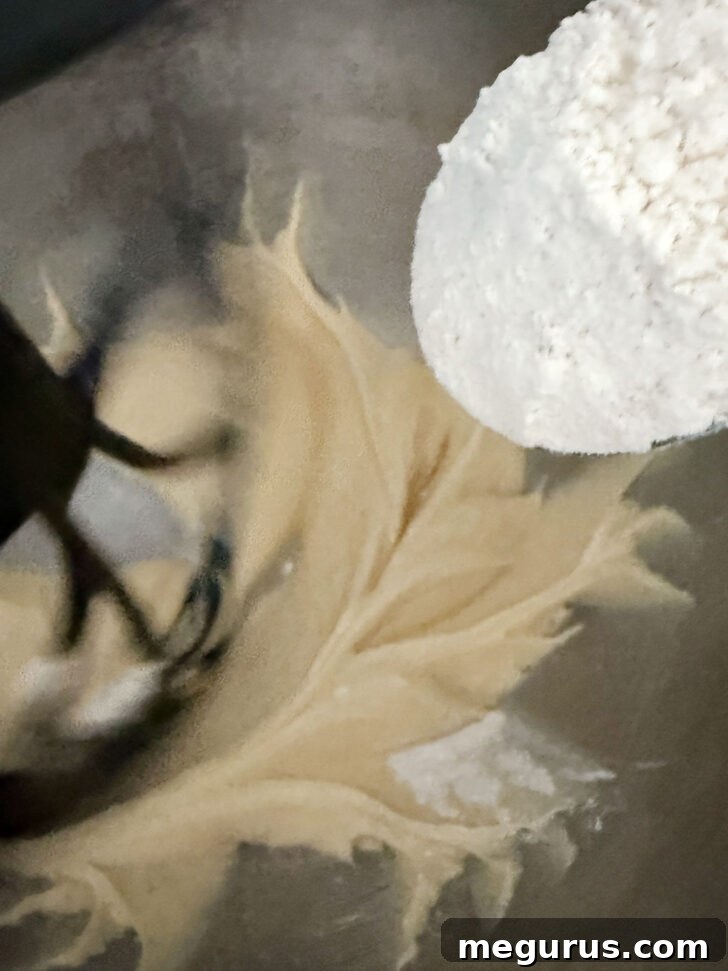 The flour mixture being added gradually to the wet ingredients in a stand mixer.