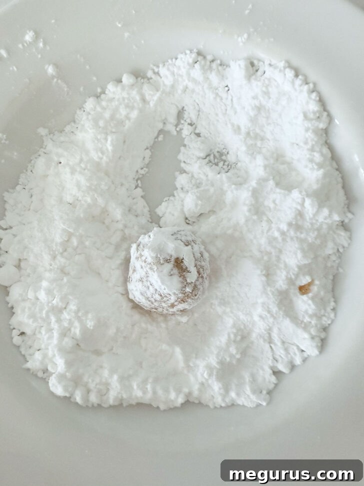 A ball of cookie dough being rolled in a bowl of icing sugar to coat it.