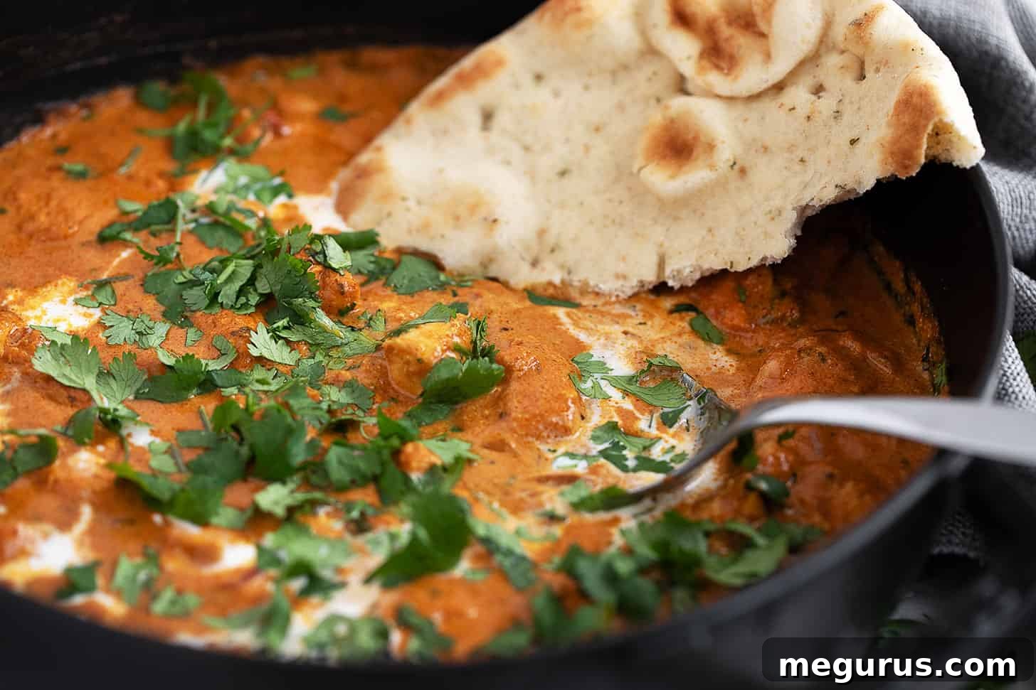 Butter chicken in a skillet with naan bread.
